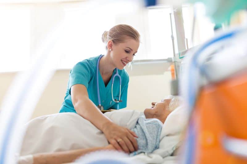 Smiling nurse positioning patient in hospital bed