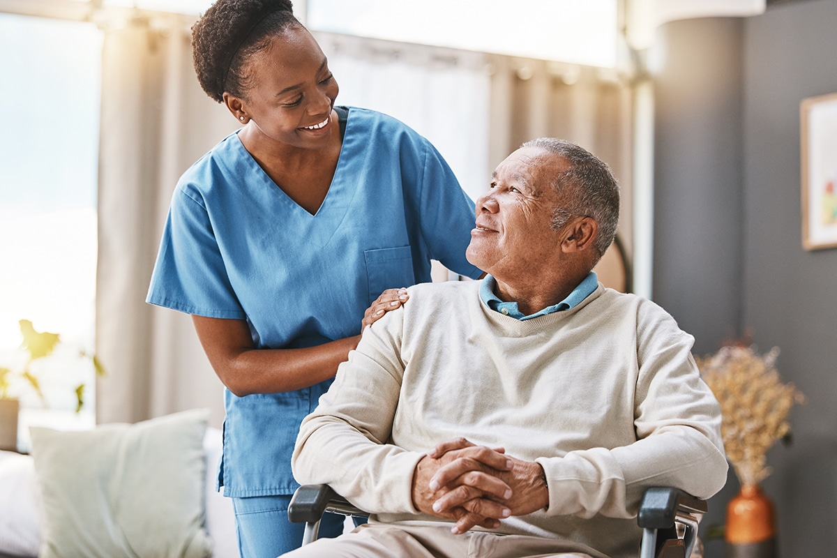 A nurse and a patient in a wheelchair are smiling together.